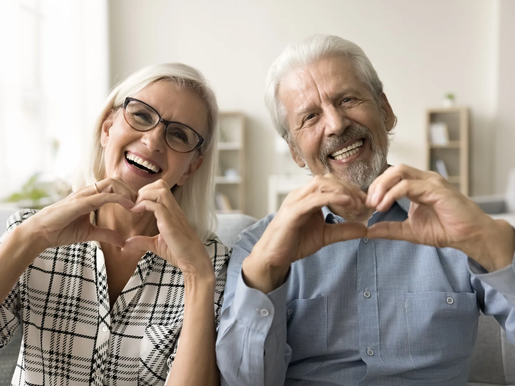 a man and a woman sitting on a couch making a heart with their hands