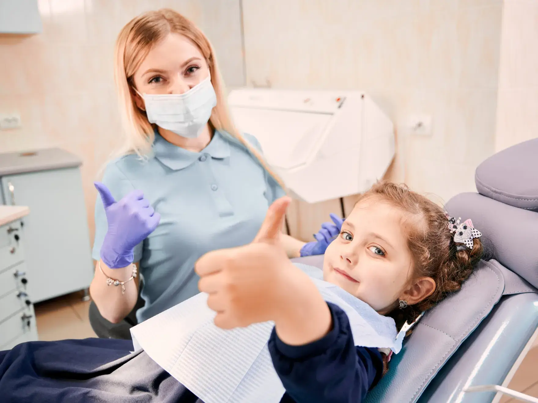 a little girl sitting in a dentist chair giving a thumbs up